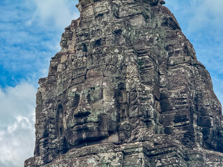 Fototapeta premium A detailed close-up of a giant, serene stone face carving on a tower at the ancient Bayon Temple in Siem Reap, Cambodia, showcasing Khmer architectural artistry and the subtle effects of time.