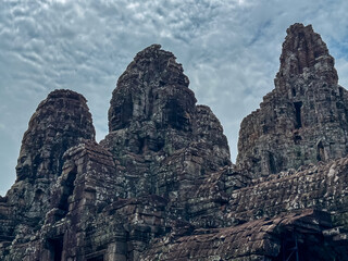 The intricately carved and weathered stone towers of magnificent Bayon temple create a complex and mysterious architectural landscape against cloudy sky in heart of Angkor Thom, Siem Reap, Cambodia