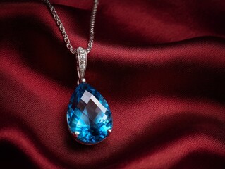 Blue topaz pendant, luxury diamond jewelry, closeup photo on deep red silk. Elegant silver chain, clear gemstone, expensive beauty concept. Beautiful blue topaz pendant.