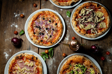Pizzas aus dem Steinofen mit Gemüse, Brokkoli, Salami, Tomate, von oben fotografiert, mit Tomaten, Basilikum und Mehl auf dem Holztisch