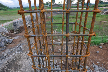 A close-up view of a reinforced steel column frame partially covered in fresh concrete at a house construction site, showing the early stage of foundation and structural work.