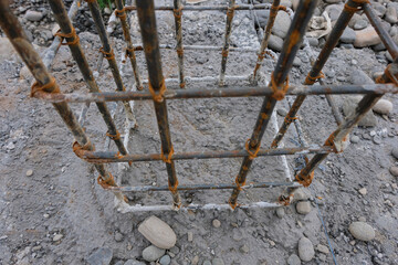 A close-up view of a reinforced steel column frame partially covered in fresh concrete at a house construction site, showing the early stage of foundation and structural work.