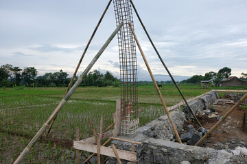 A close-up view of a reinforced steel column frame partially covered in fresh concrete at a house construction site, showing the early stage of foundation and structural work.