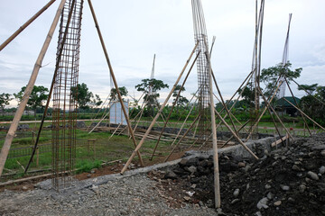 A close-up view of a reinforced steel column frame partially covered in fresh concrete at a house construction site, showing the early stage of foundation and structural work.
