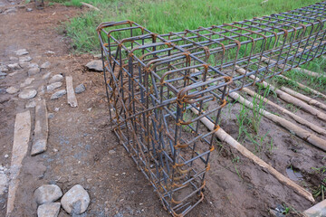 A close-up view of a reinforced concrete footing structure, commonly known as a “cakar ayam” foundation, made of steel rebar arranged in a grid pattern at a residential construction site