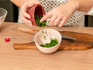A woman transfers freshly chopped parsley into a small bowl. Preparing fresh herbs for salad or a home-cooked dish.