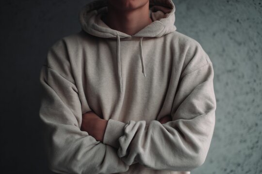 Torso of person wearing beige hoodie with crossed arms against textured wall with minimalist aesthetic, demonstrating fashion. - Powered by Adobe
