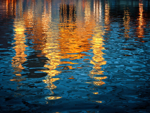 Vibrant golden and blue abstract reflection patterns shimmering on rippling water surface during twilight or sunset ambiance - Powered by Adobe