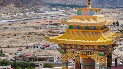 Obraz premium Panoramic view to Leh valley with airport runway through intricate carved golden roof of Buddhist prayer wheel pavilion or Mani wheel for sacred spin. Ladakh Region, India