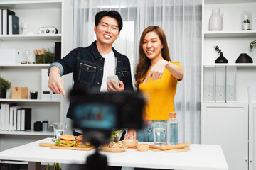 Chef influencers reading comment on phone for answer time on social media cooking show channel live streaming menu dish mix salad, bun bread wholegrain and hamburger record by video camera. Infobahn.