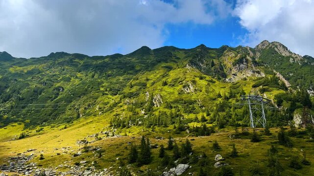 Emerald greenery of the vegetation covering the slope of the beautiful mountains. Support of the funicular located on the hill. The Carpathian Mountains, Romania.