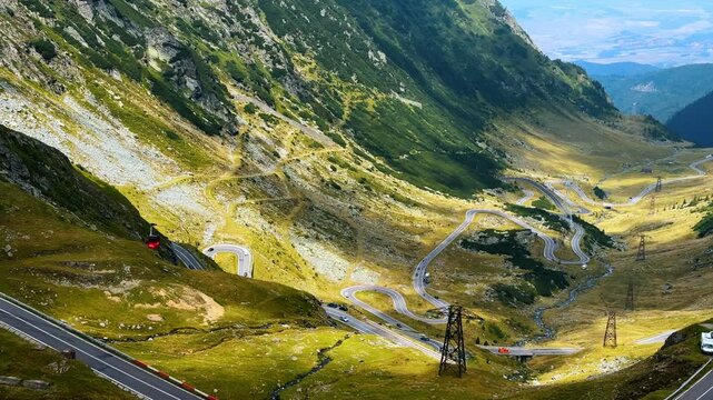 Red funicular cabin descends into the valley. Admiring the spectacular Transfagarash highway in the Carpathian Mountains, Romania. Aerial view.