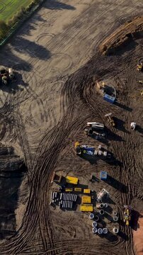 Vertical drone video of a new housing development under construction, showing foundations, machinery, and building materials from above. Modern residential site captured in bright daylight.