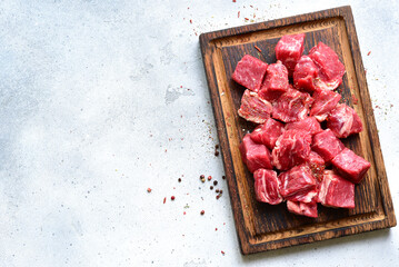 Cubes of raw organic meat ( beef or lamb ) on a wooden cutting board . Top view with copy space.