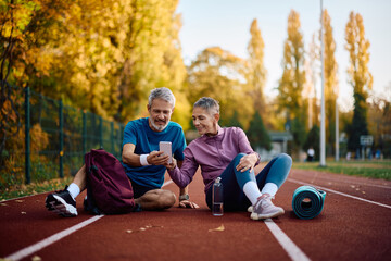 Mature sports couple using app on cell phone while exercising in autumn park.