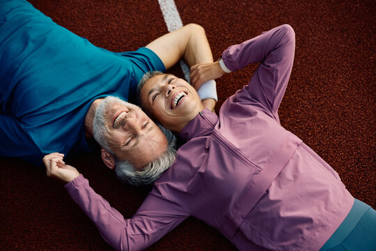 Above view of cheerful mature sports couple relaxing on running track.