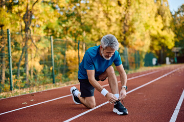 Mature runner tying his shoelaces while preparing for sports training outdoors.