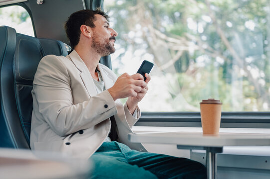 Man traveling by train, using smartphone, drinking coffee - Powered by Adobe