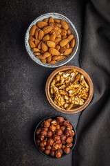 Peeled walnut, hazelnut and almond kernels in bowls on black table. Top view.