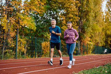 Mature sports couple running during outdoor workout in autumn.