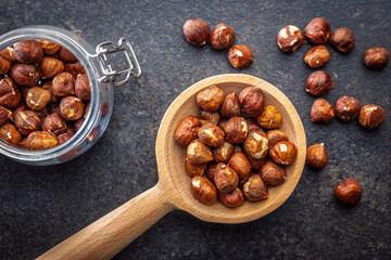 Peeled hazelnut kernels on wooden spoon on black table. Top view.