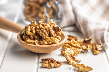 Peeled walnut kernels on wooden spoon on white table.