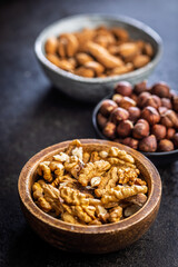Peeled walnut, hazelnut and almond kernels in bowls on black table.