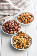 Peeled walnut, hazelnut and almond kernels in bowls on white table.