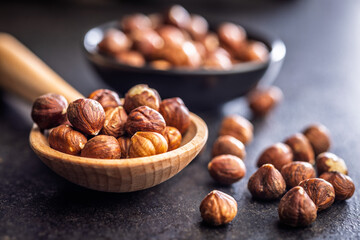 Fototapeta premium Peeled hazelnut kernels on wooden spoon on black table.