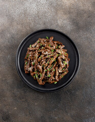 Stir-fry beef marinated with teriyaki sauce, green onions and sesame seeds on a dark background. Top view. 
