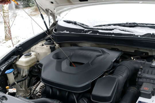 Close-up side view of auto mechanic man checking engine oil level in car, workshop, garage. car repairing service with open hood,outside backyard in winter.