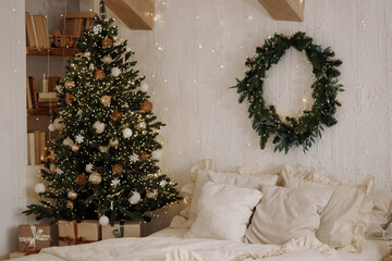 Scandi loft bedroom with beige bedding, wooden beams, Christmas tree and wreath on a textured white wall. Warm holiday decor suitable for seasonal themes, home comfort and winter atmosphere.