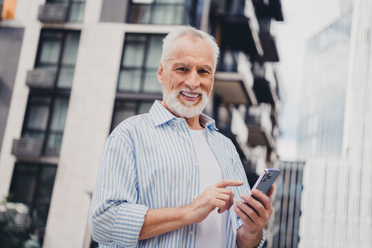 Senior man using phone in city street with modern buildings smiling outdoors in business casual attire for stock photography - Powered by Adobe