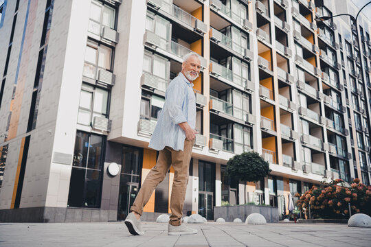 Elderly man walking through a modern urban residential complex smiling during a sunny day in a contemporary cityscape with balconies stroll