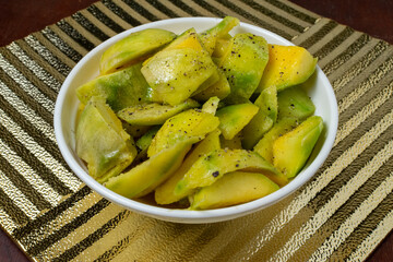 Bowl of Sliced Green Unripe Mango Seasoned with Salt, Lemon Juice and Black Pepper on Textured Gold Placemat