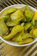 Bowl of Sliced Green Unripe Mango Seasoned with Salt, Lemon Juice and Black Pepper on Textured Gold Placemat