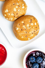 Healthy Continental Breakfast Flat Lay with Multigrain Buns, Granola with Blueberries, Orange Juice and Fruit Jams on White Background