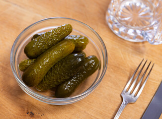 There is ceramic bowl filled with pickled cucumbers on table. Crispy, sourly salted pickled cucumbers, serving options, table decoration ideas