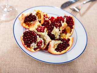 Pieces of ripe pomegranate with juicy seeds on a white plate top view