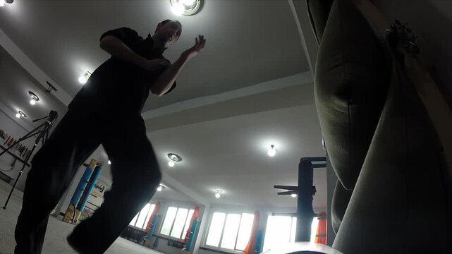 Two focused men wearing black martial arts uniforms train Wing Chun Kung Fu by rhythmically striking canvas wall bags side by side in a traditional training studio.

