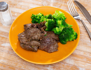 Cooked chicken liver with spices and broccoli on an orange plate. Nutritious protein dish for lunch