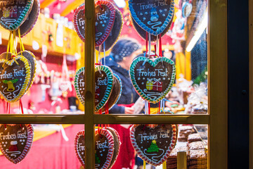 Fototapeta premium A festive christmas market stall viewed through a wooden window, decorated with hanging gingerbread heart cookies with colorful icing messages. 
