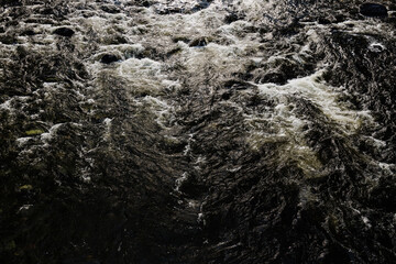 Textura abstracta de la turbulenta y espumosa agua oscura del Río Santo Domingo, capturada en El Carmen de Viboral, Antioquia, Colombia. Movimiento, fluidez y poder de la naturaleza.