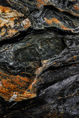 Patrón abstracto y texturizado de roca metamórfica mojada en colores negros, ocres, naranjas y blancos, encontrada en el Río Santo Domingo, El Carmen de Viboral, Antioquia.