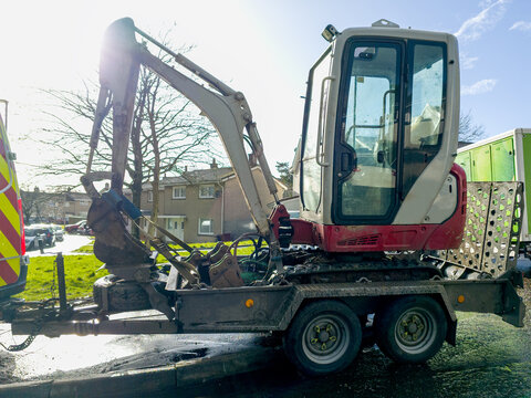 An excavator on a trailer,  used for groundworks, maintenance, with a van. mini excavator  used for trenching, drainage, stump removal, and general excavation tasks. Loaded on a small, robust trailer.