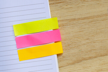Colorful sticky page markers on a notebook page and a wooden desk.