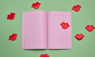 An open notebook with blank pink pages surrounded by red lip appliques on a green background
