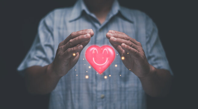 Emotional care concept. A person gently holding a glowing heart icon with a smiling face. Symbolizing kindness, compassion, support, positivity and mental well-being in a modern digital style.