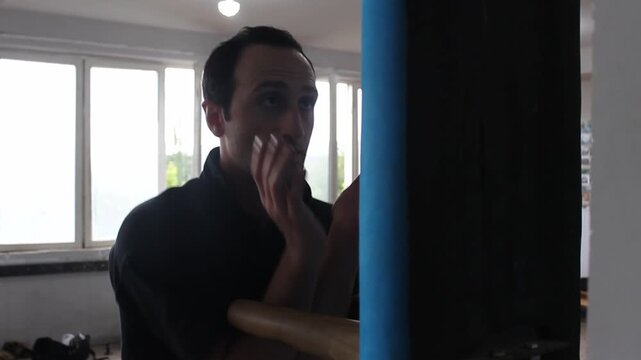 A professional martial artist wearing a black uniform is practicing Wing Chun techniques on a blue wooden dummy inside a traditional Chinese martial arts training studio.

