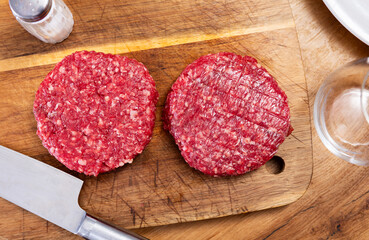 Two juicy beef patties are laid out on cutting board, semi-finished product is ready for use and frying. Burger patties